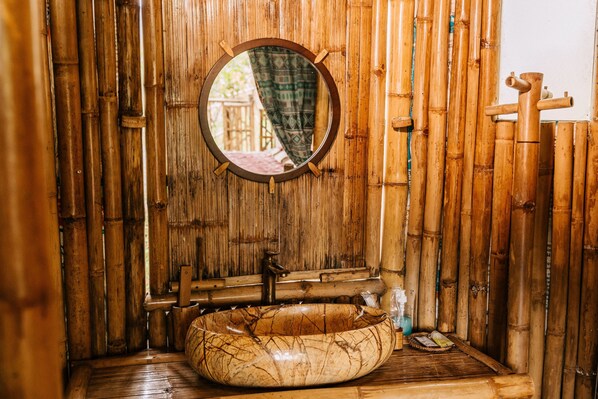 Un baño con un espejo redondo, un lavamanos de madera y paredes de bambú.