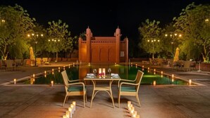 An outdoor dining area with a table set for two, surrounded by candles, and a decorative pool in the background. - Gaj Kesri by 7Apple Resorts  (Bikaner)