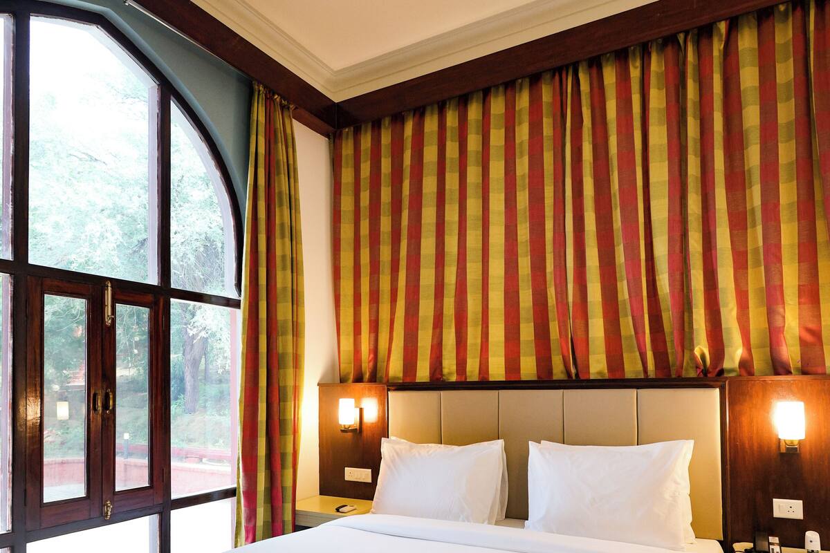 Una cama grande con cabecera, dos lámparas de noche y un ventanal con cortinas.