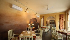 A dining area with wooden tables and chairs, air conditioning units, and decorative lighting. - Gaj Kesri by 7Apple Resorts  (Bikaner)
