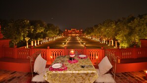 A table set for two with a candle, surrounded by a red railing and trees. - Gaj Kesri by 7Apple Resorts  (Bikaner)