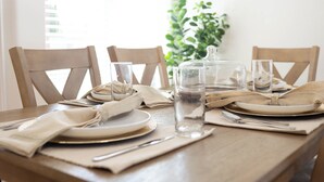 Une table à manger est dressée avec des assiettes, des verres et des couverts. On y trouve également une bouteille d’eau et un bocal en verre.