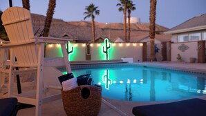 Un espace aménagé au bord de la piscine, avec un fauteuil de relaxation, un panier en osier et un panneau lumineux en forme de cactus.