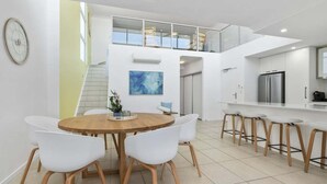 A modern kitchen with a stainless steel refrigerator, white cabinetry, and a wooden dining table with white chairs. - The Lookout Retreat - Woorim (City of Moreton Bay)