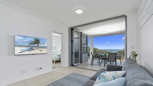 A modern living room with a grey sofa, a patterned rug, and a painting of a beach scene. - The Lookout Retreat - Woorim (City of Moreton Bay)