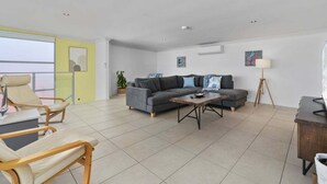 A modern living room with a grey sofa, beige armchairs, a wooden coffee table, and a TV stand. - The Lookout Retreat - Woorim (City of Moreton Bay)