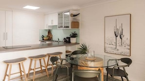A modern kitchen with white cabinets, a central island with stools, and a cactus-themed artwork on the wall. - Carmine - Fiesta Palms (Byron Bay)