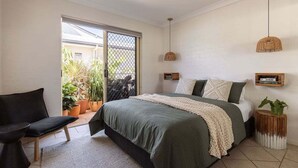 A bedroom with a bed, a chair, a small table, and a potted plant. - Carmine - Fiesta Palms (Byron Bay)