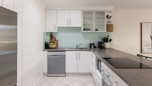 A modern kitchen with white cabinets, a dishwasher, and a countertop with a sink. - Carmine - Fiesta Palms (Byron Bay)