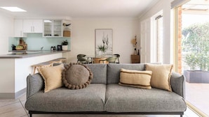 A modern living room with a grey sofa, a dining table, and a kitchen area. - Carmine - Fiesta Palms (Byron Bay)