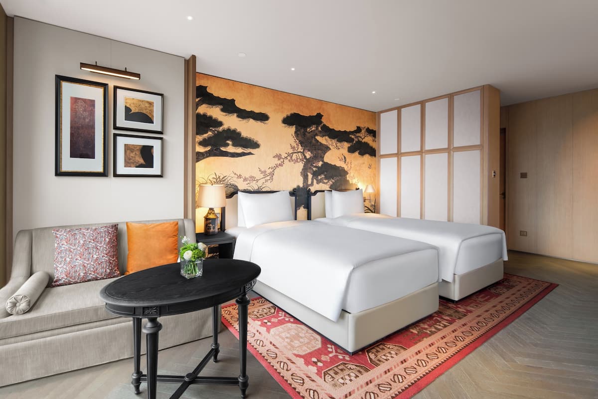 A hotel room with a bed, a sofa, a small table, and a wall with artwork.