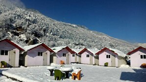 Une rangée de petites cabanes à un seul étage, avec des toits rouges, entourées d’un paysage enneigé et avec une montagne en arrière-plan.