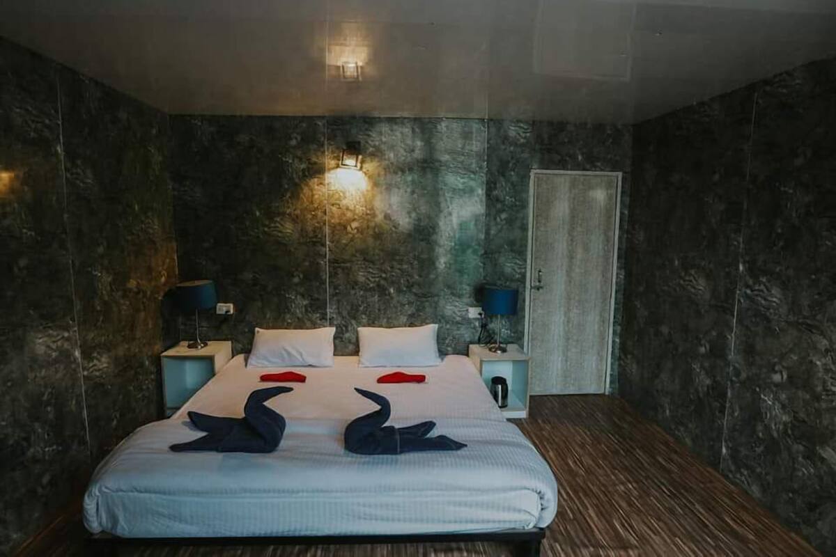 Un dormitorio con una cama, dos mesitas de noche, una lámpara de pared y una puerta.