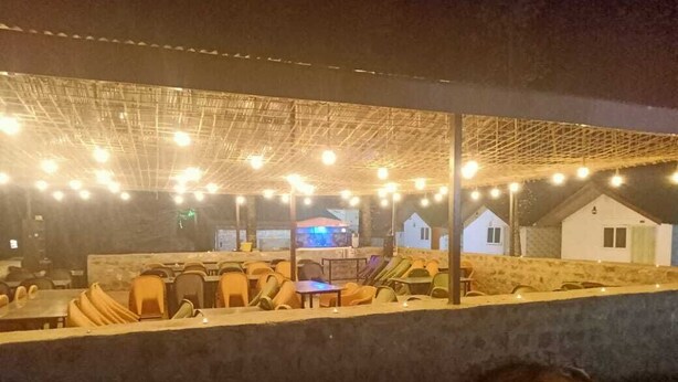 Un espace extérieur aménagé avec des tables et des chaises, une zone couverte décorée de guirlandes lumineuses, et un bâtiment visible au fond.