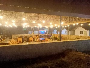An outdoor seating area with tables and chairs, a covered section with string lights, and a building in the background.
