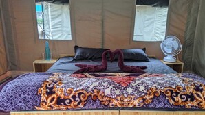 Une chambre avec un lit, deux tables de chevet, un ventilateur fixé au mur et deux fenêtres avec des rideaux.