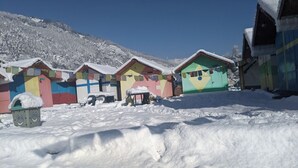 Une rangée de cabanes colorées, recouvertes de neige, avec une chaîne de montagnes en arrière-plan.