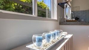 Cocina con una encimera que muestra cuatro recipientes de vidrio transparente llenos de arena azul, un lavamanos y una ventana con vistas a la vegetación.