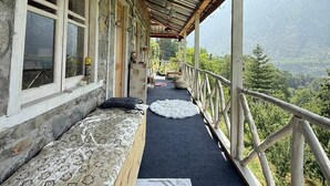 A rustic wooden balcony with a stone wall, a wooden bench, and a view of a mountainous landscape. - KALA STUDIO AND STAY (Kullu)