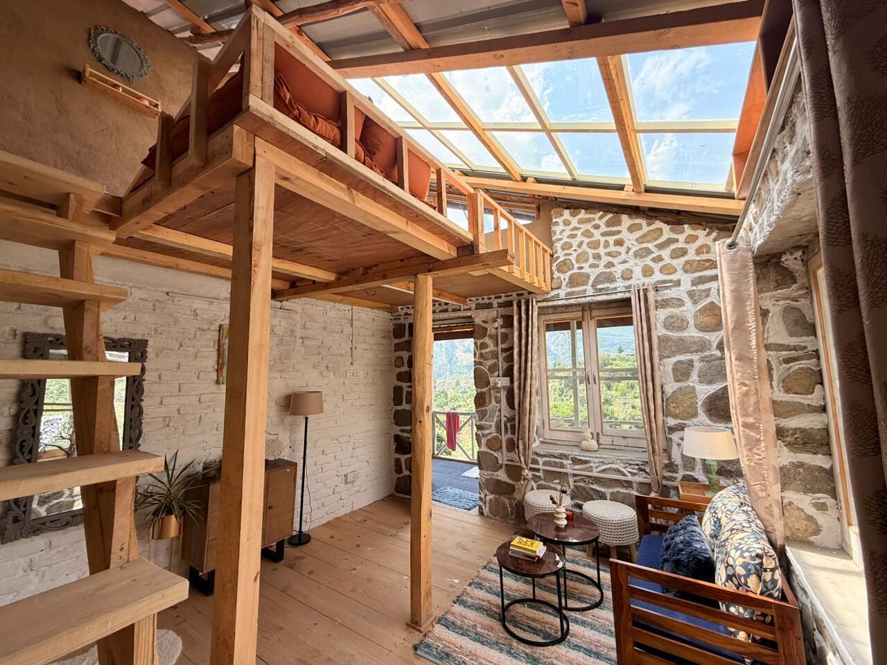 A rustic interior with a loft bed, stone walls, wooden beams, and a skylight.