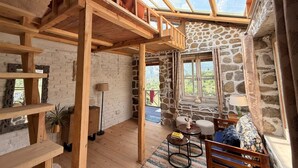 A rustic interior with a loft bed, stone walls, wooden beams, and a skylight. - KALA STUDIO AND STAY (Kullu)