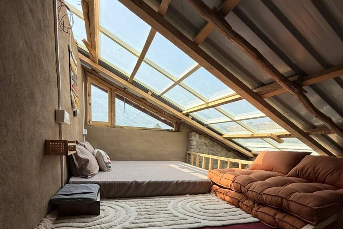 A cozy attic bedroom with a skylight, a bed, a sofa, and a rug.