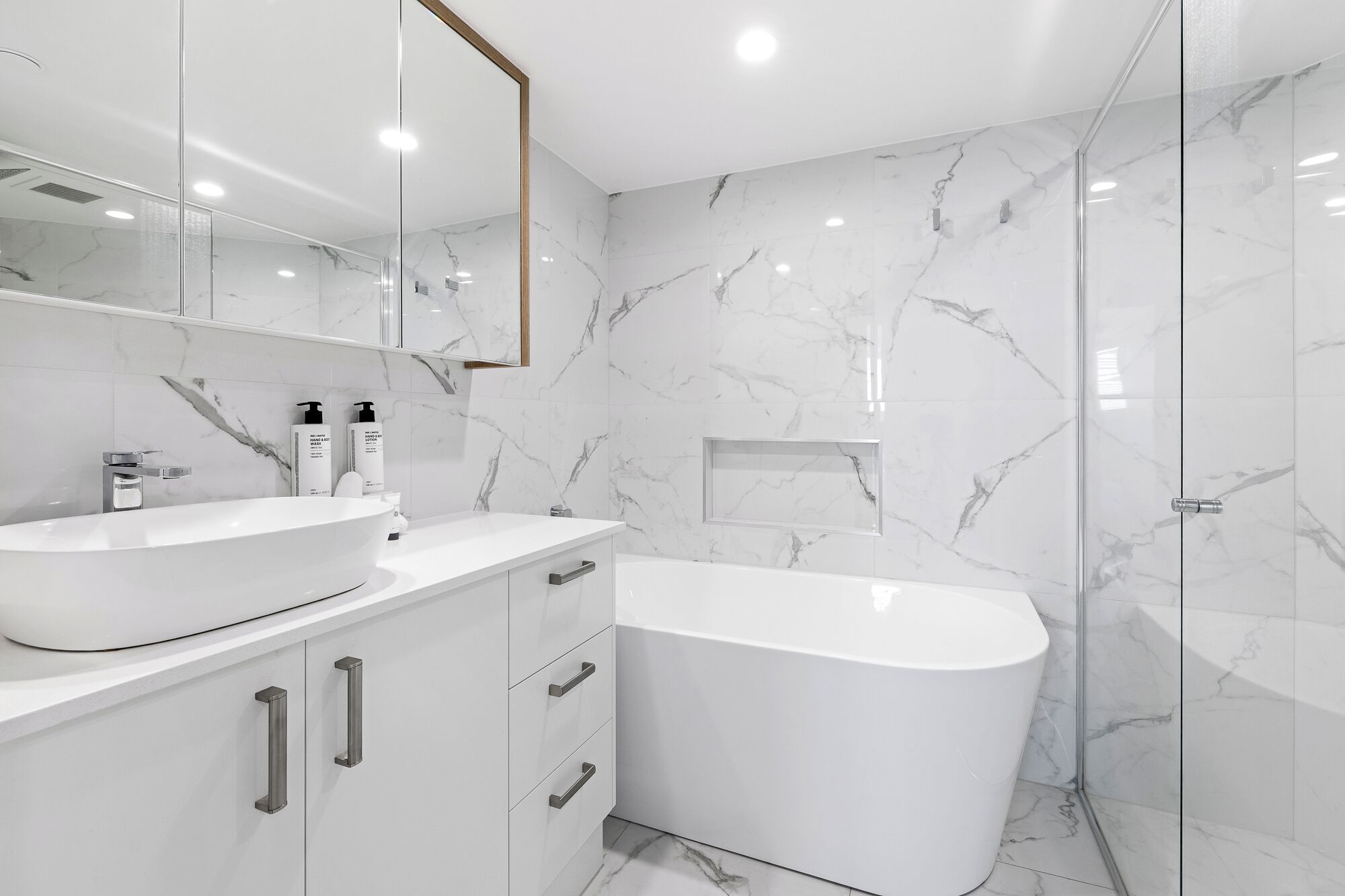 Un baño moderno con una bañera independiente, un espejo grande y paredes de mármol.