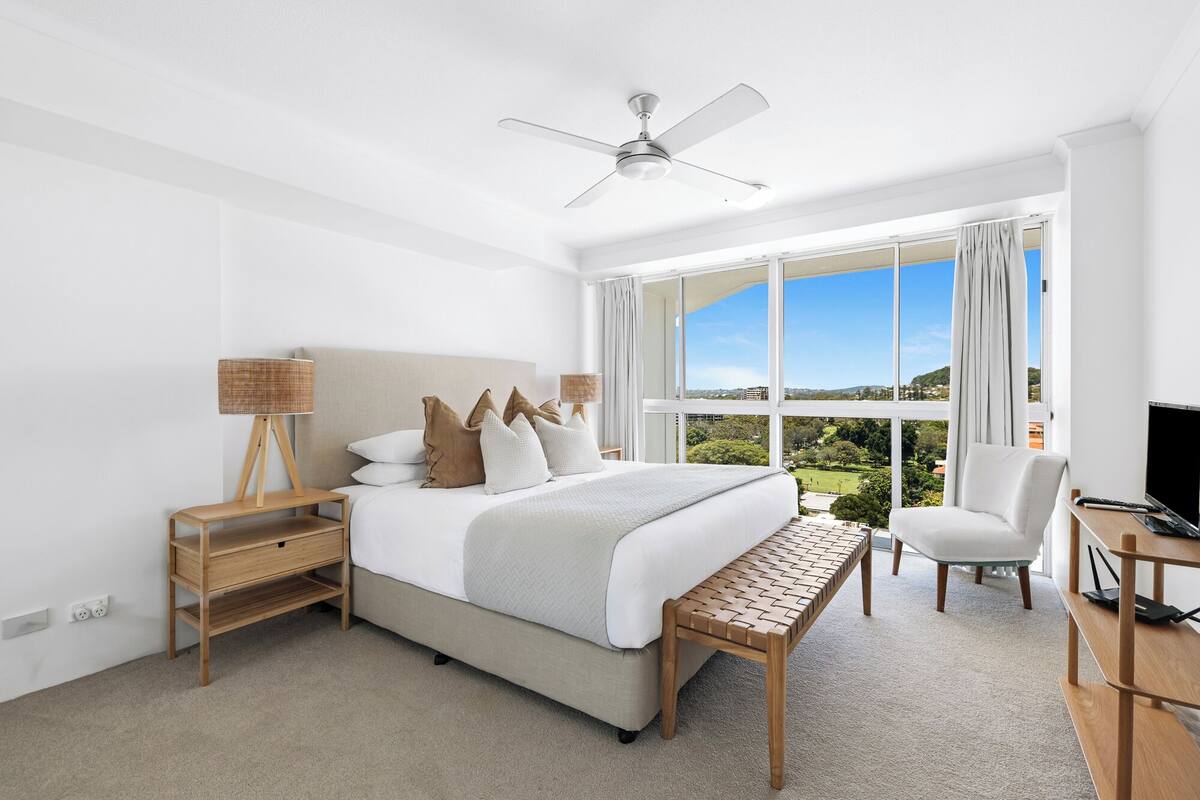 Une chambre moderne avec un grand lit, un bureau, une chaise et une vue sur l’extérieur.