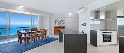 Una cocina moderna con una isla central, un comedor con sillas de madera y vista al océano.