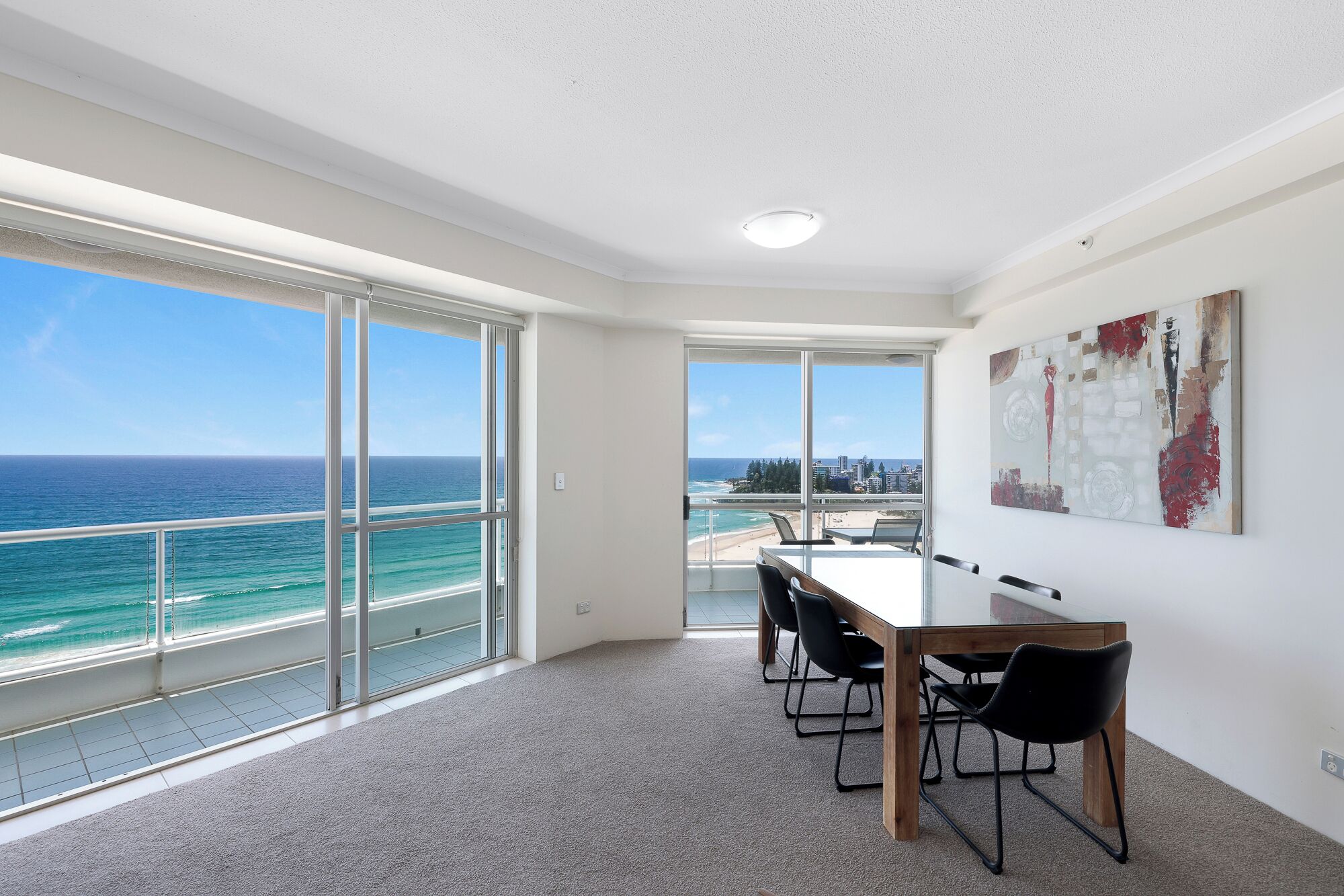 A room with a large sliding glass door leading to a balcony with a view of the ocean and city skyline.