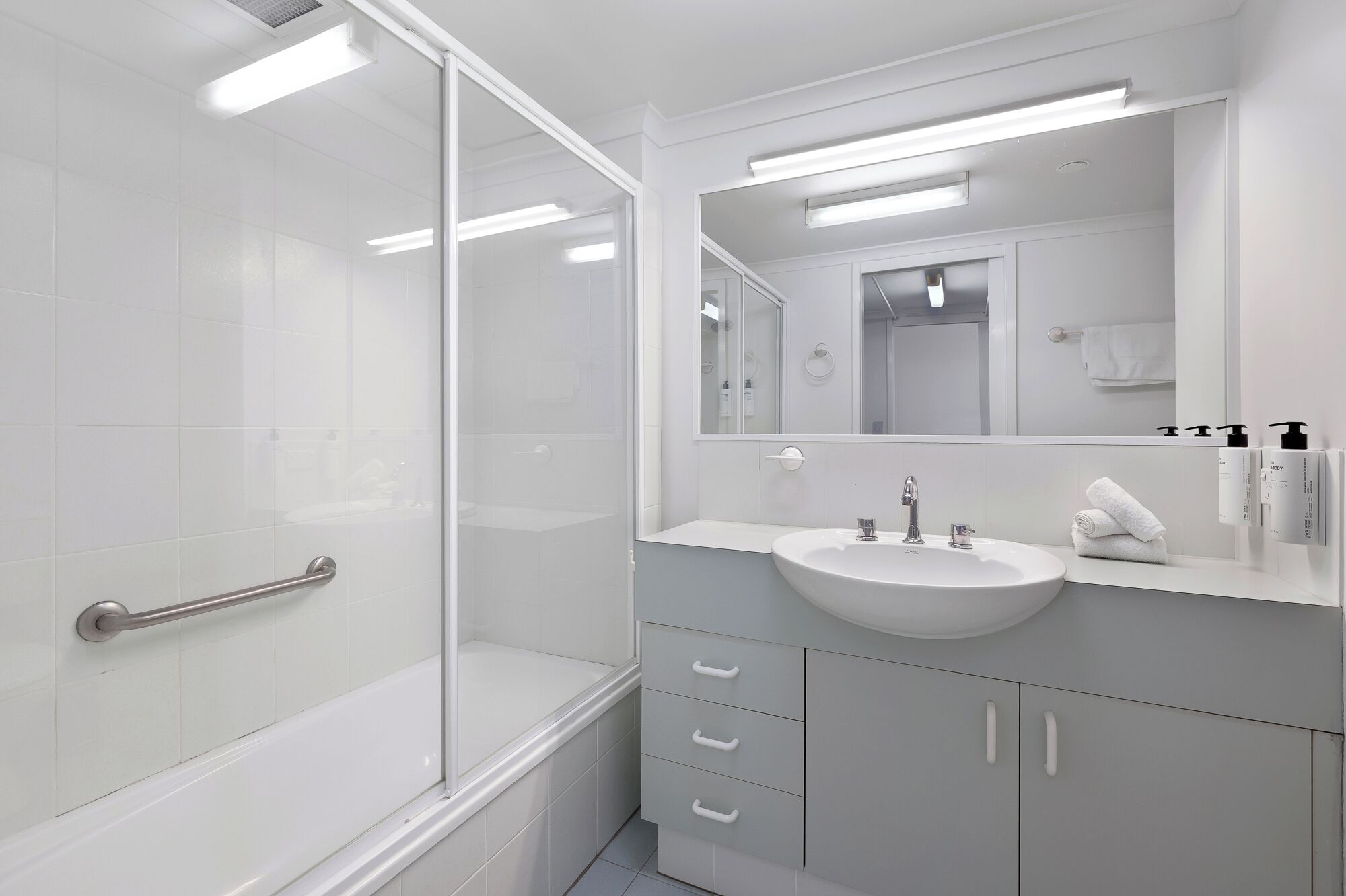 Un baño moderno con cabina de ducha de vidrio, lavamanos blanco y un espejo grande.