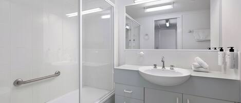 Un baño moderno con cabina de ducha de vidrio, lavamanos blanco y un espejo grande.