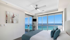 A hotel room with a bed, a ceiling fan, a large window with a view of the ocean, and a painting on the wall. - ULTIQA Points North (Queensland)