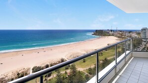 A beach view from a balcony with a clear sky, sandy beach, and distant buildings. - ULTIQA Points North (Queensland)