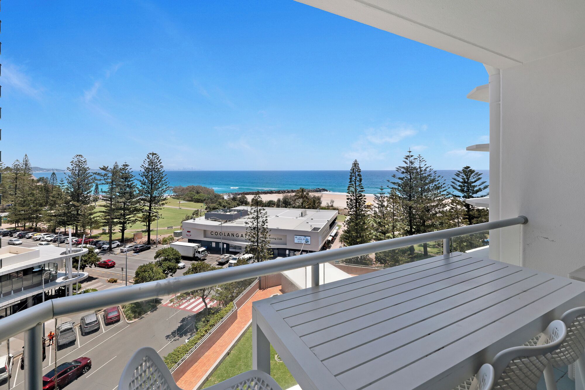 A balcony with a view of the ocean, a parking lot, and buildings in the background.