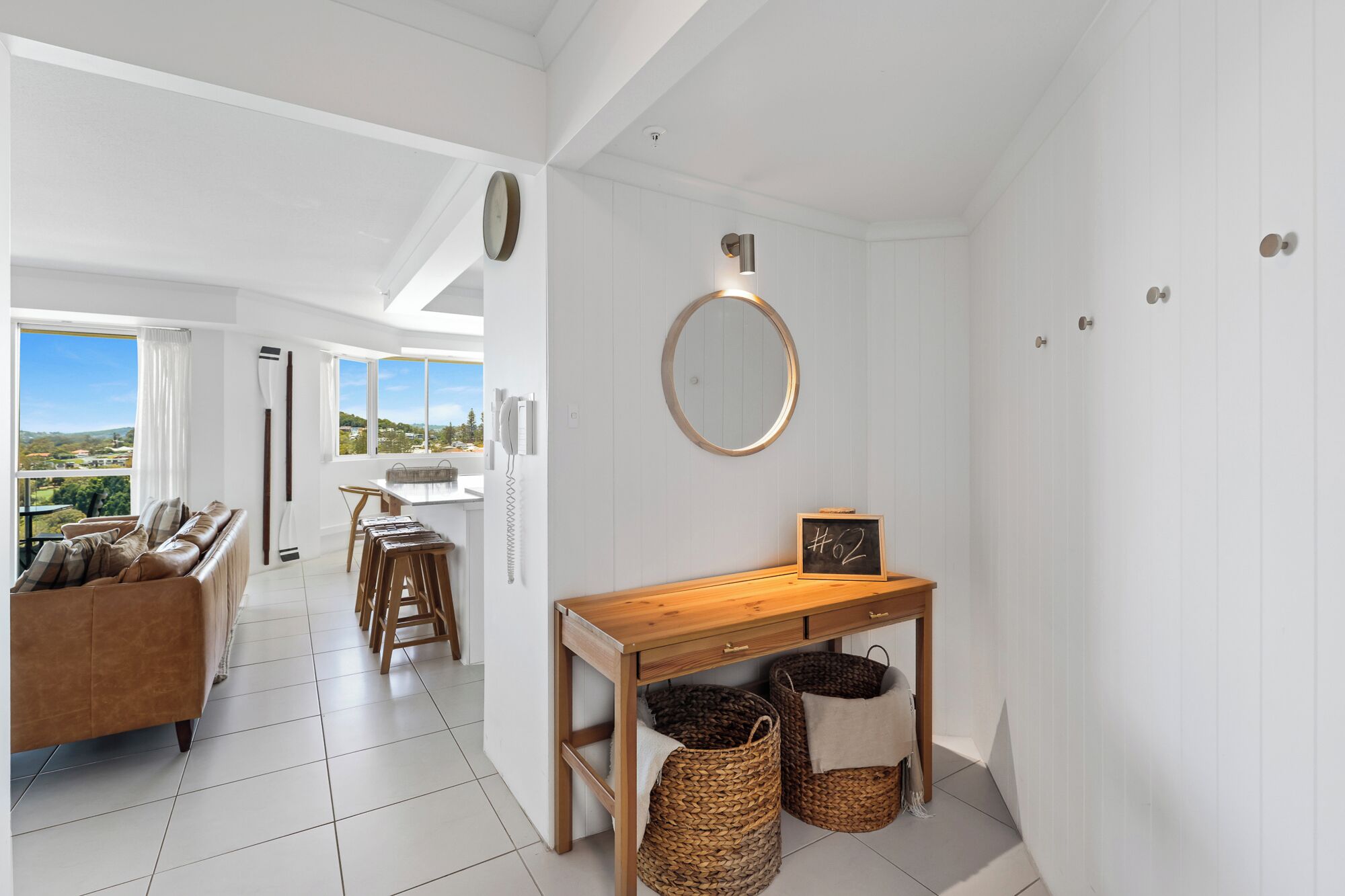 A modern kitchen with a wooden table, two wicker baskets, and a round mirror on the wall.