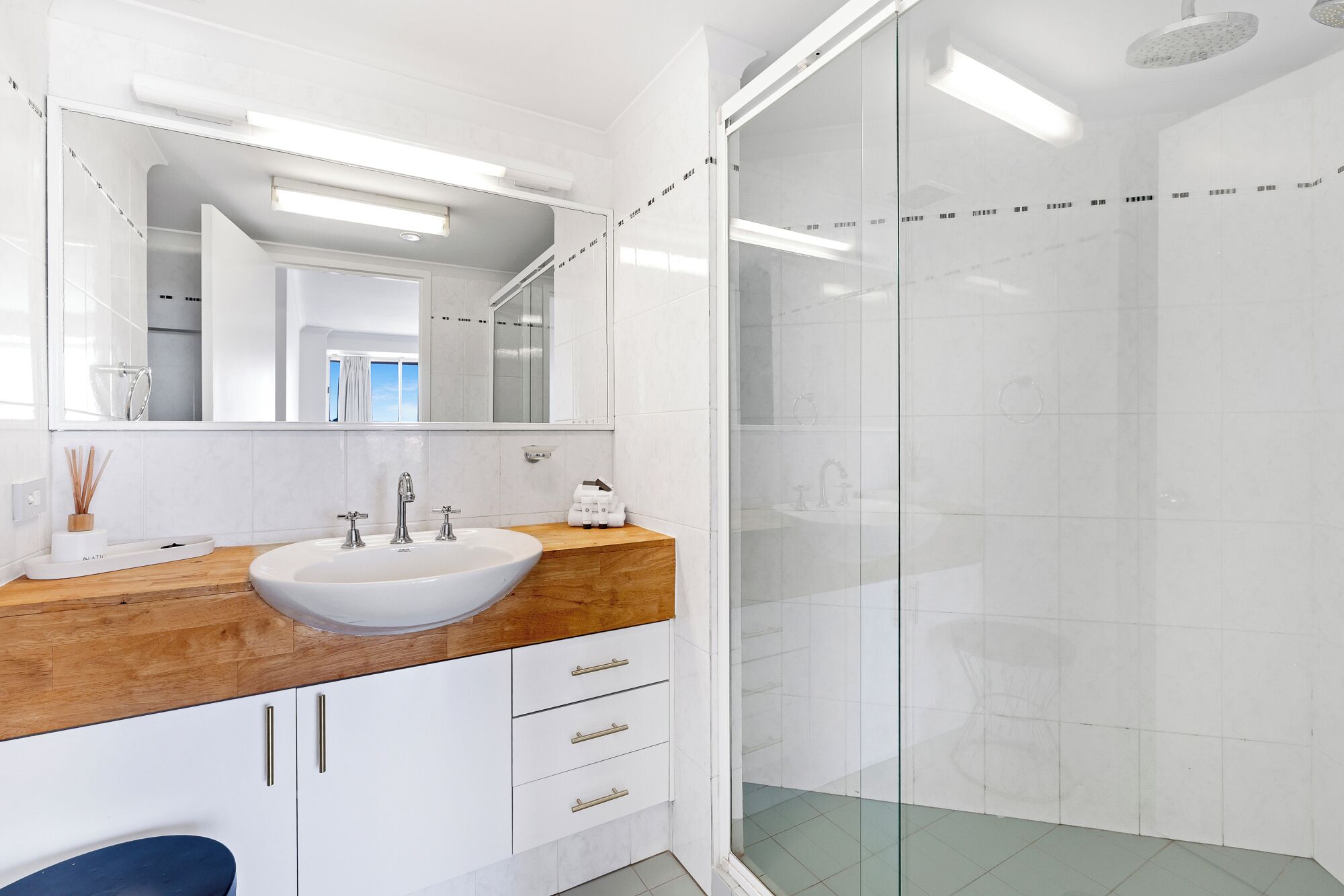 Un baño moderno con lavamanos blanco, encimera de madera y cabina de ducha de vidrio.