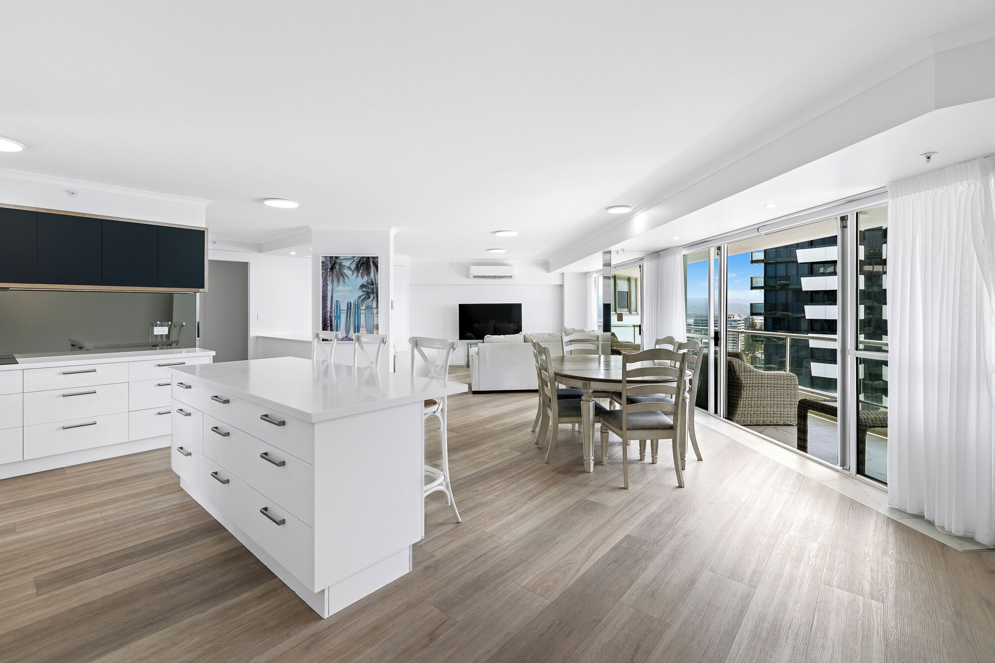 Una cocina moderna con armarios blancos, una isla central y un comedor con un amplio ventanal que ofrece vistas a la ciudad.