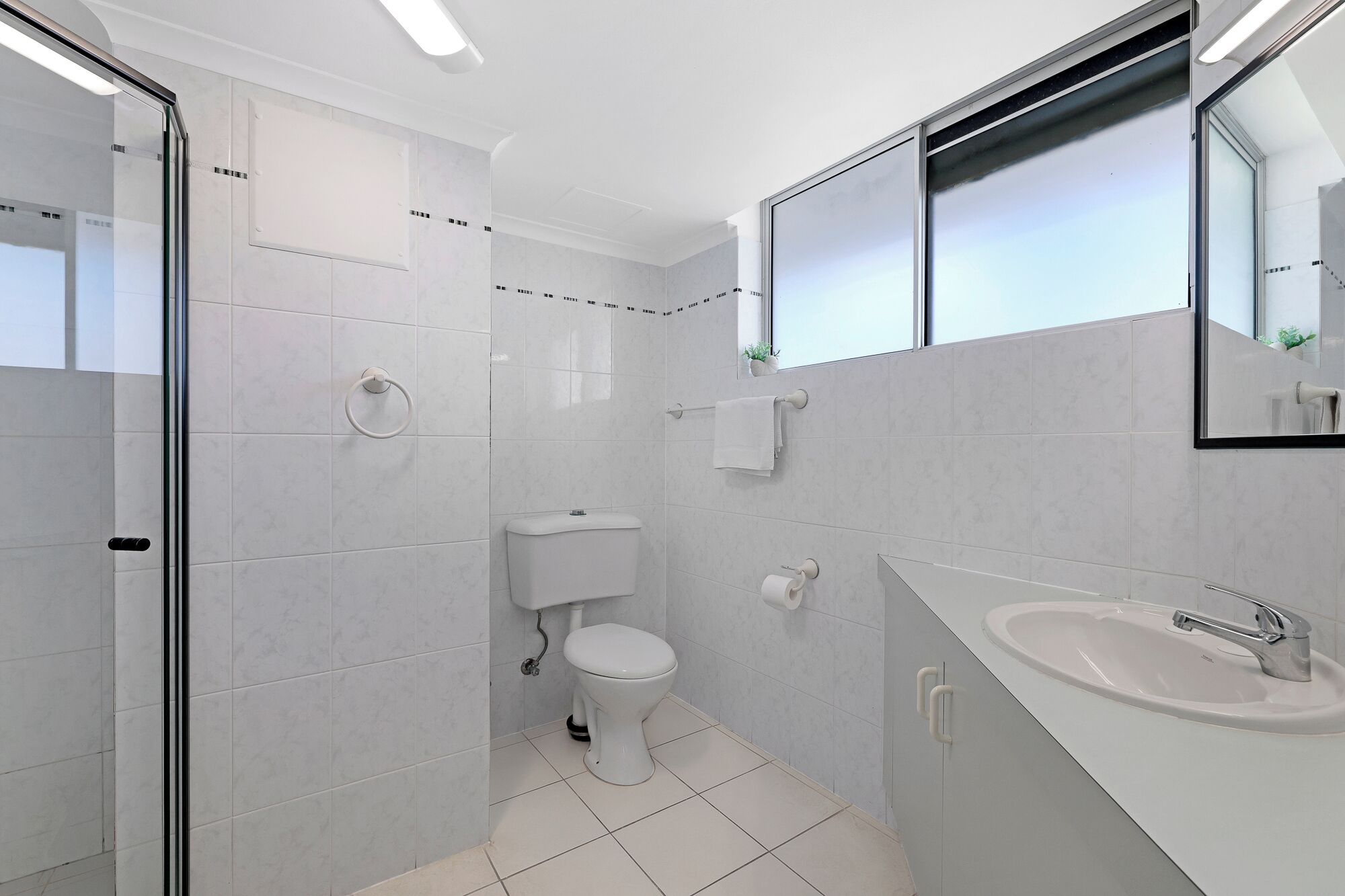 A modern bathroom with a toilet, sink, and glass shower enclosure.