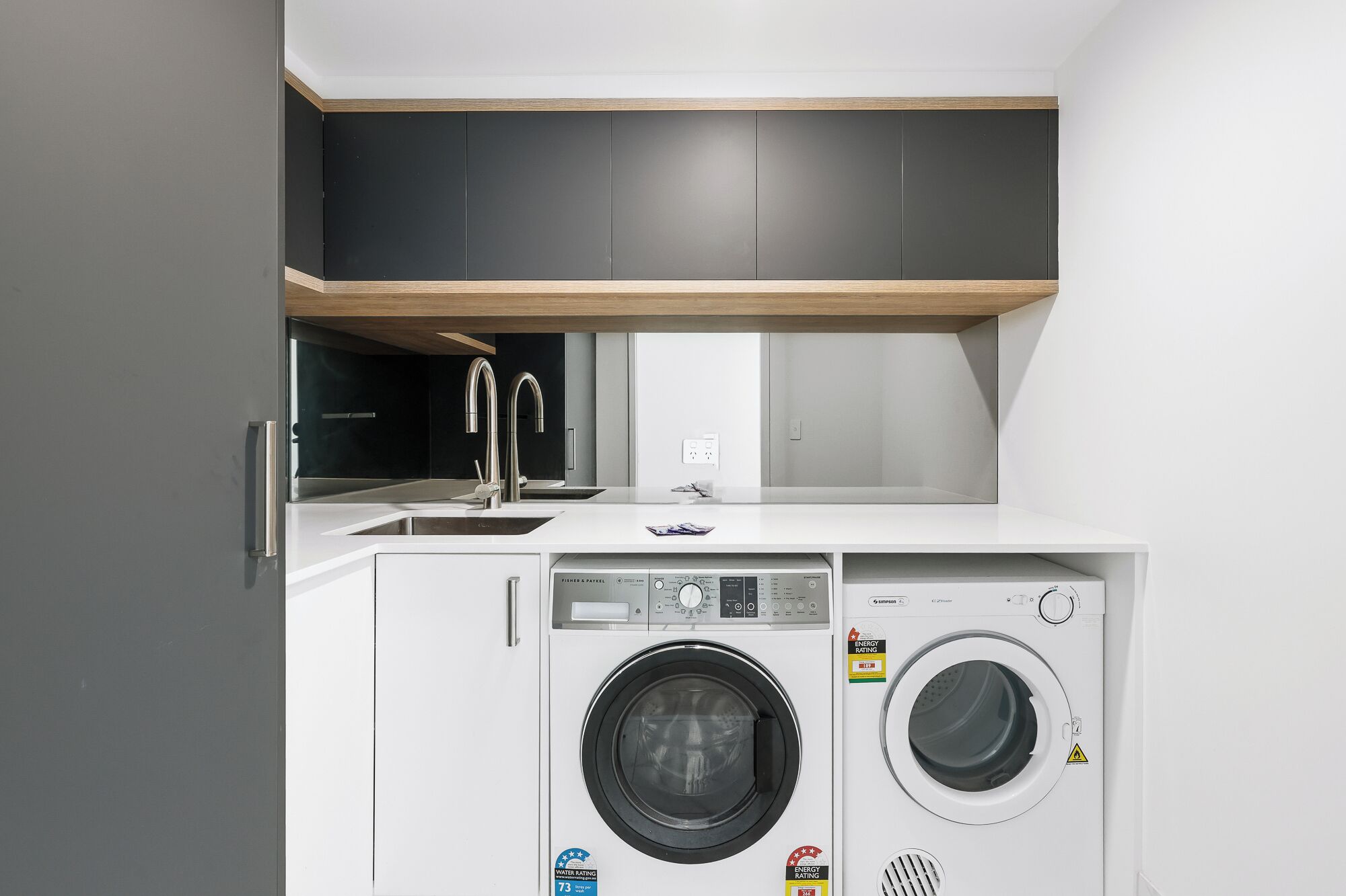 Ein kleiner Waschbereich mit Waschmaschine und Trockner, einem Waschbecken und einem darüberliegenden Schrank.
