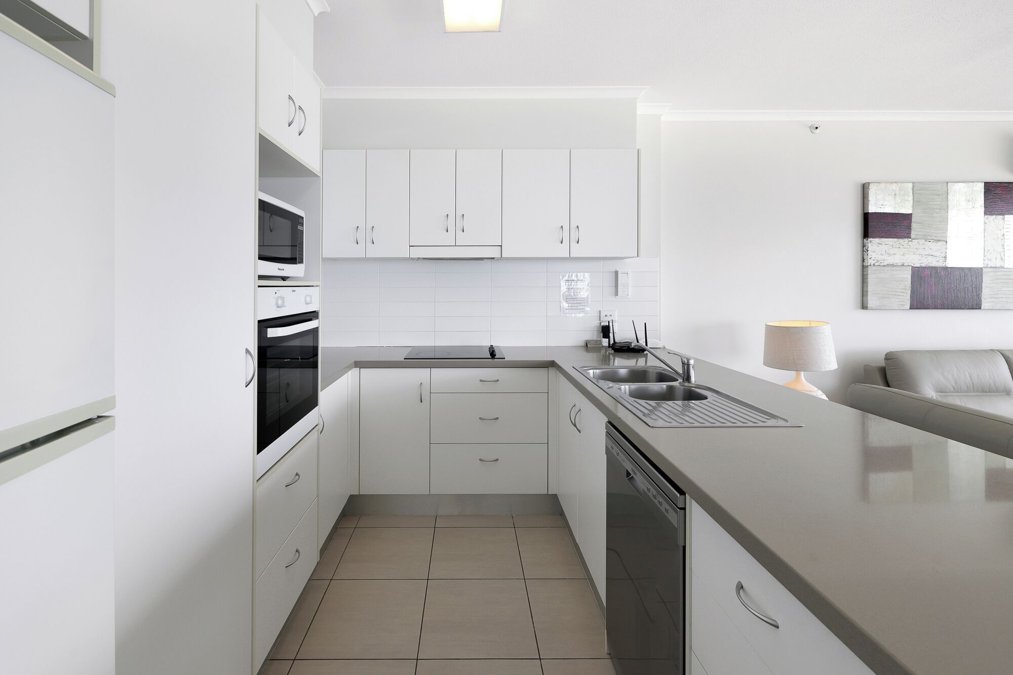 A modern kitchen with white cabinetry, a built-in oven, a dishwasher, and a large island with a sink.