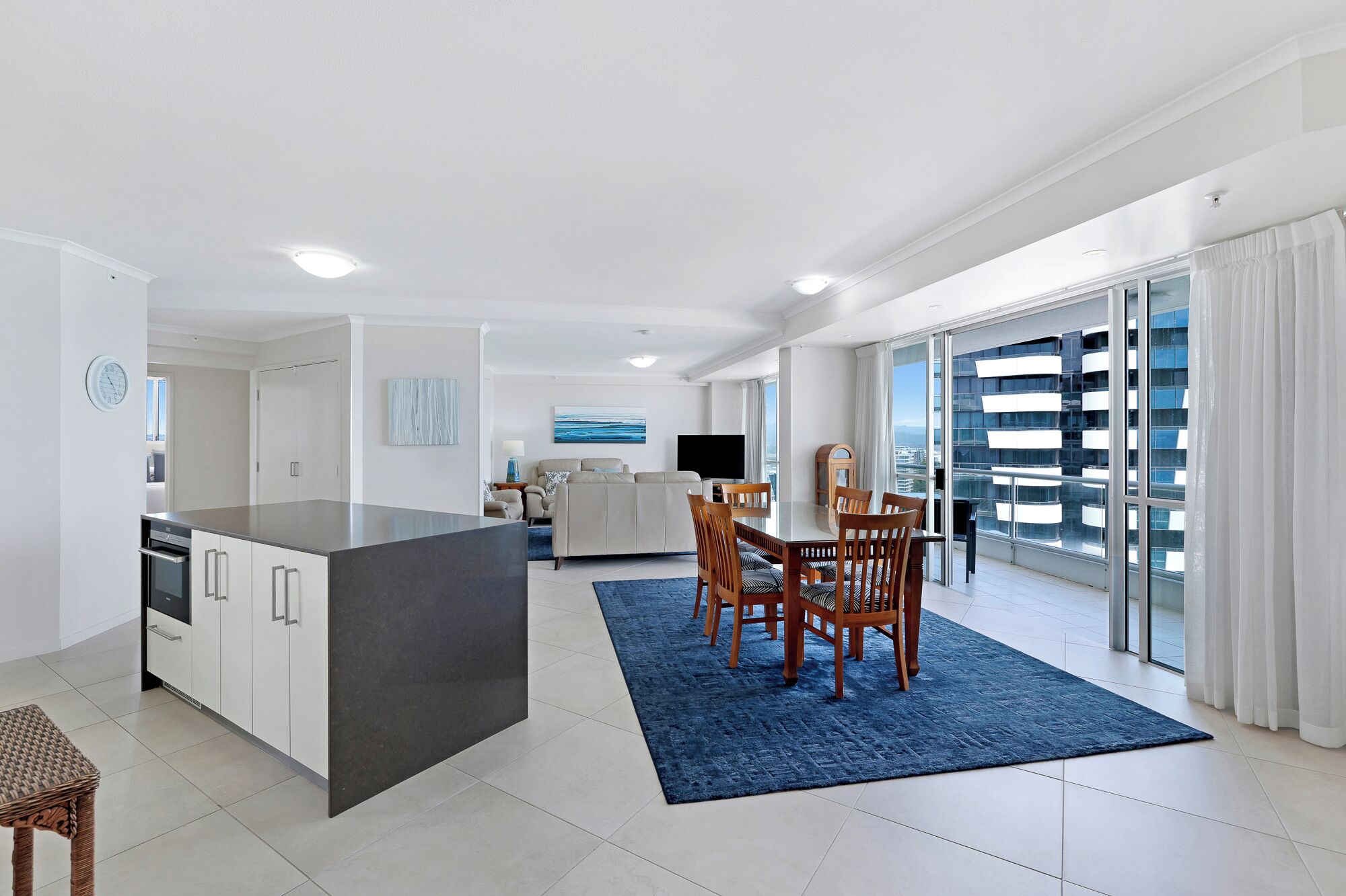 A modern apartment with a kitchen, dining area, living room, and a balcony with a city view.