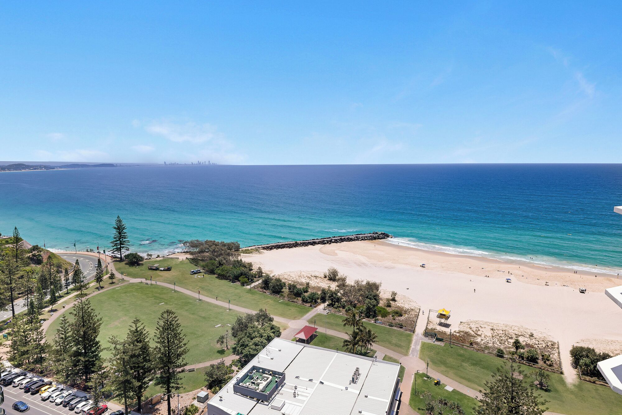 A coastal view with a beach, a parking area, and a building with a flat roof.