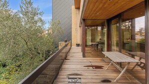 A wooden deck with a table and chairs, a glass door leading to a room, and a view of trees. - ’t Zandhuis - vintage stay with garden in Ostend (Oostende)
