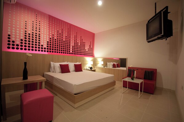 A modern bedroom with a large bed, bedside tables, a red sofa, a TV, and a decorative wall panel. - OK Resort Laemchabang (Si Racha)