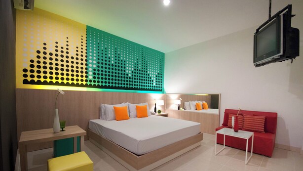 A modern hotel room with a large bed, a red sofa, a small table, and a TV mounted on the wall. - OK Resort Laemchabang (Si Racha)