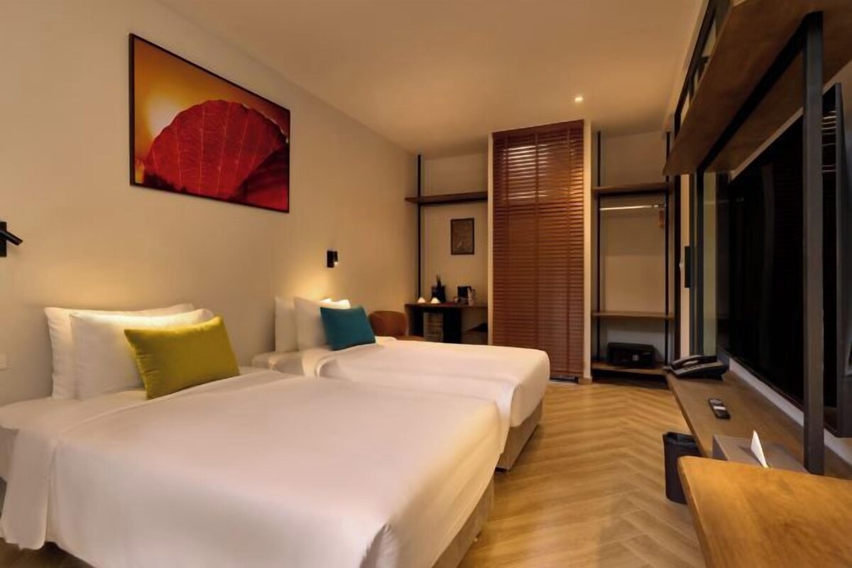 A hotel room with two beds, a large window, a wooden floor, and a wall-mounted artwork.