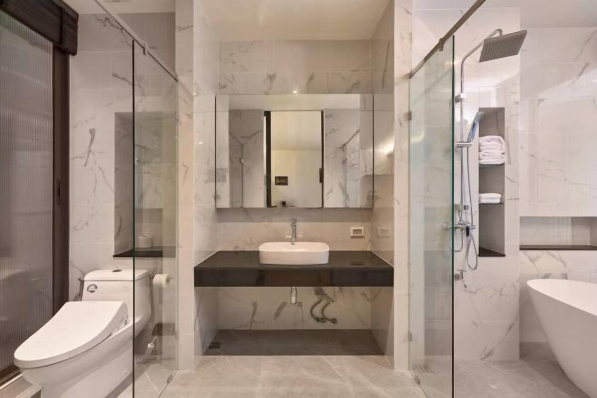 A modern bathroom with a glass-enclosed shower, a white toilet, and a large bathtub.
