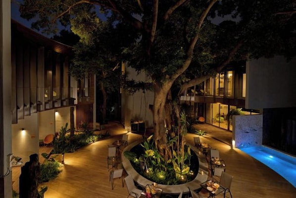 A courtyard with a large tree, outdoor seating, and a swimming pool. - Red Door Hotel, Bangkok (Bangkok)