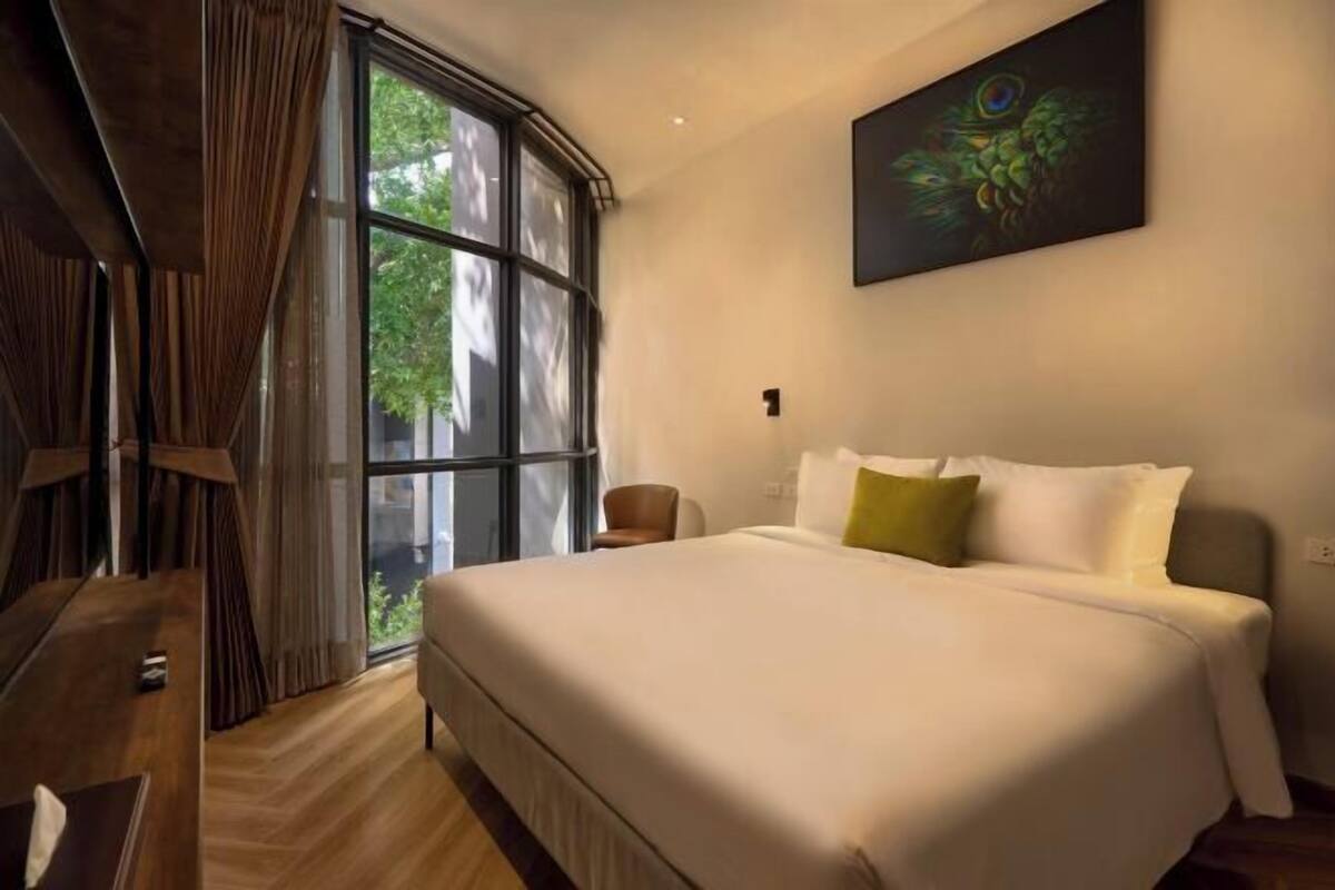A hotel room with a large bed, a window with curtains, a painting on the wall, and a wooden floor.